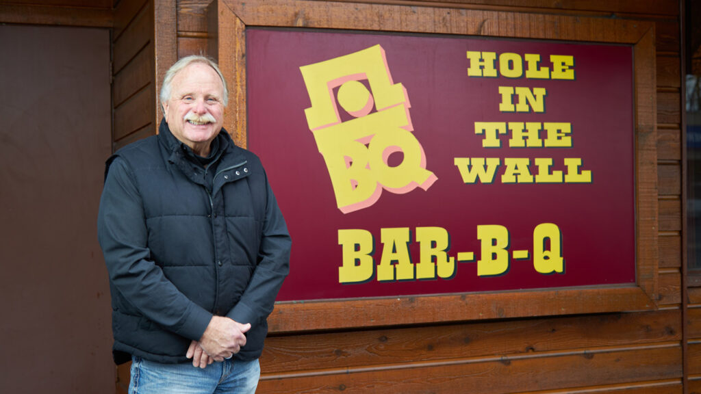 BBQ owner stands next to his sign.