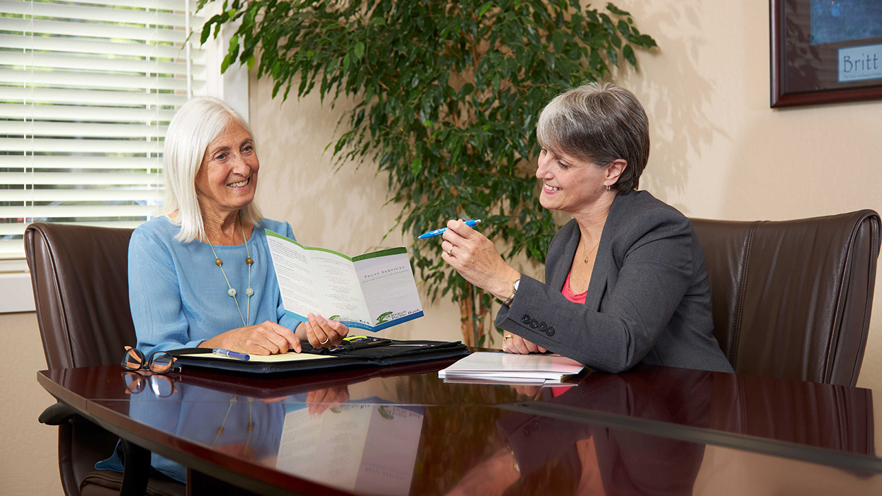 Two women sit in conference room, discussing solo aging.